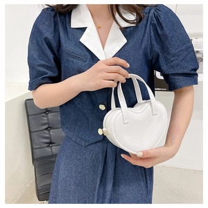 Detail of white heart-shaped mini handbag with glossy finish and gold zipper hardware