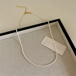 Détail du collier de petites perles blanches avec fermoir mousqueton doré et chaîne