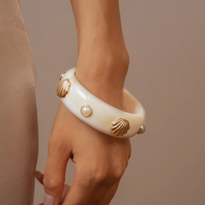 Détail d'un bracelet en résine crème avec accent de coquille dorée et perle intégrée