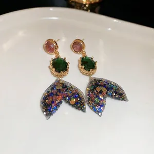 Elegant gold mermaid tail drop earrings with pink and green crystal studs in ceramic tray