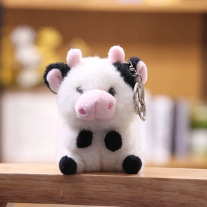 Primer plano de llavero de vaca de peluche blanco y negro con orejas rosas y anillo de metal