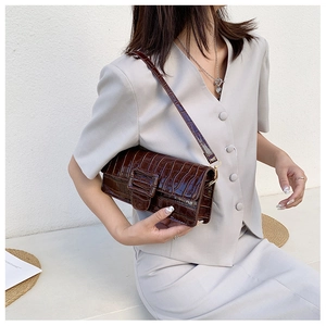 Detail of dark brown croc-embossed shoulder bag featuring metal hardware and fine leather texture