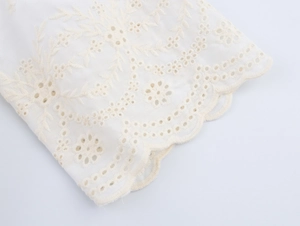 Détail de la broderie florale blanche et des motifs ajourés sur le bord de la manche