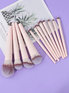 Flat lay of 13 professional pink makeup brushes with soft synthetic hair on purple surface