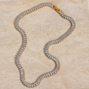 Detail shot of luxury gold tennis necklace with emerald-cut zircon stones on marble base