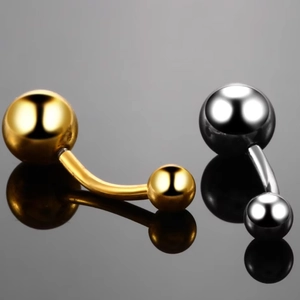 Golden and silver curved barbell belly rings with sparkling crystals on reflective surface
