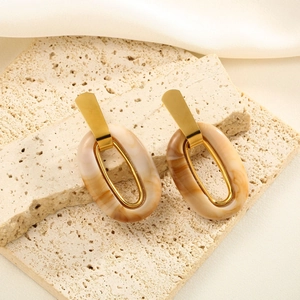 Detail view of gold hoop resin earrings with marble pattern on a natural beige stone