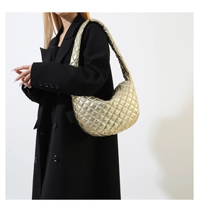 Close-up of golden metallic quilted cloud bag worn by a model in a black winter coat