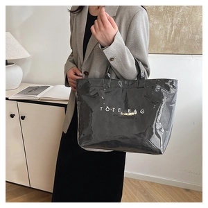 Minimalist black glossy tote bag featuring white TOTE BAG text shown in a stylish home setting