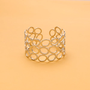 Wide silver hollow geometric bangle with circular patterns on a soft orange background