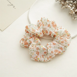 Close-up of floral print scrunchie in orange and yellow on a cream fabric base