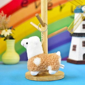 Close-up of a cute plush alpaca keychain with soft curly fur texture hanging on a stand.