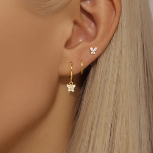 Detail of gold butterfly earrings with white zircon stones worn on the ear