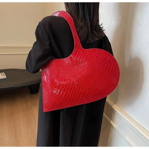 Detail of red heart-shaped shoulder bag with glossy crocodile texture on a model