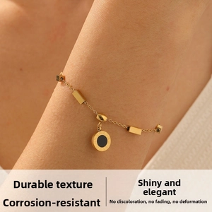 Close-up of gold-plated bracelet featuring a Roman numeral coin pendant and black onyx detail