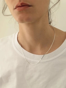 Primer plano de un collar de cadena de serpiente cuadrada dorada minimalista en una modelo