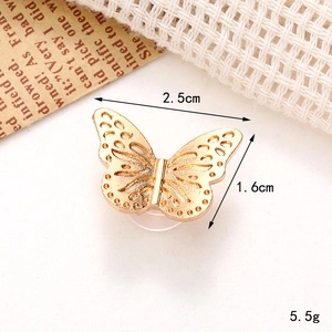 Detail of a hollow gold butterfly shoe charm with dimensions on textured fabric background