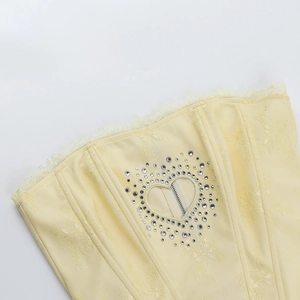 Détail d'un haut en dentelle jaune clair avec découpe cœur en strass et fermeture éclair métal