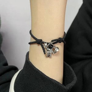 Close-up of black braided couple bracelet with silver astronaut and heart charms