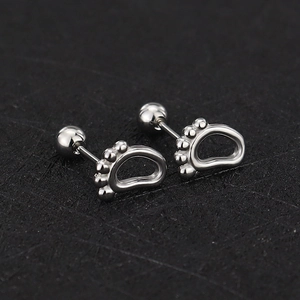 Detail view of silver screw-back animal paw stud earrings on black textured surface