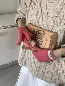 Close-up of pink knit fingerless gloves held by person in beige sweater with paper bag