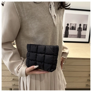 Chic black quilted clutch bag featuring puffy grid stitching held by a model in a cozy setting