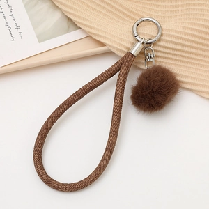 Détail d'un porte-clés en tissu tressé marron avec pompon en peluche et crochet en argent