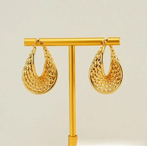 Macro view of gold droplet earrings featuring intricate woven texture and hoop design