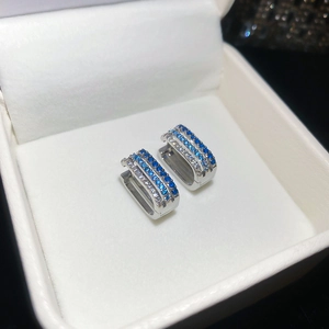 Close-up of silver hoop earrings with blue and clear zircons in a white jewelry box