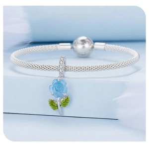 Macro shot of silver charm bracelet with blue rose pendant and green enamel leaf detail