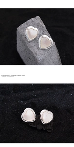 Detail view of heart-shaped silver stud earrings with white glossy inlay on dark stone