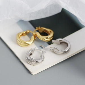 Detail of twisted C-shaped earrings in polished gold and silver finishes on elegant paper