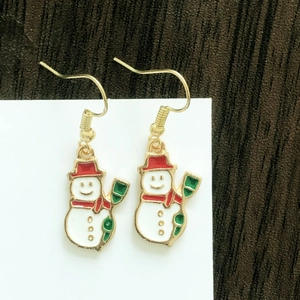 Detail shot of snowman earrings with red and green enamel on a wooden background