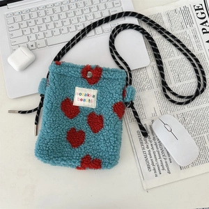 Close-up of blue fleece crossbody bag with red hearts and woven strap on a desk