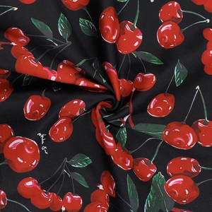 Detailed close-up of textile fabric featuring red cherry prints on a black background