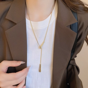 Close-up of golden teardrop pendant necklace worn with professional blazer and white tee