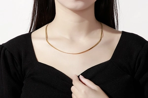 Gros plan d'un collier chaîne serpent dorée sur un mannequin en haut à col en V noir