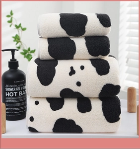 Macro shot of fluffy cow-print coral fleece towel set stacked in a modern bathroom