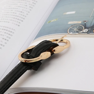 Close-up of a slim black leather belt with a stylish interlocking gold metal buckle