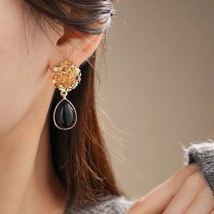 Detail of vintage flower stud earrings with black waterdrop pendants worn by a model