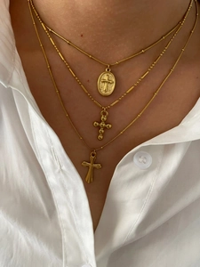 Close-up of triple layered gold titanium steel cross necklaces on a female model wearing white