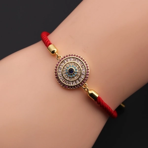 Detail of red braided evil eye bracelet with gold plating and blue crystals on a wrist