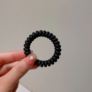 Close-up of matte black spiral telephone wire hair tie held by hand on beige background