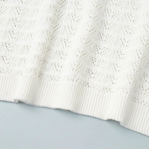 Detail shot of white knitted fabric with hollow geometric patterns and ribbed hem design