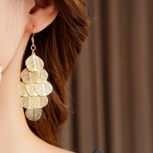 Detail view of gold layered hollow leaf tassel earrings worn on a model's ear