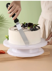 Detail of a stainless steel spatula smoothing cream on a white rotating cake turntable