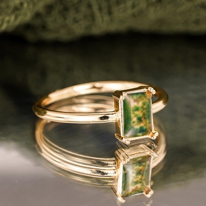 Macro shot of rectangular green moss agate ring in gold setting on mirror surface