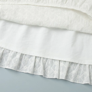 Vue macro de l'ourlet de robe blanche avec broderie en losange et bords à volants