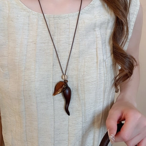 Retro resin wood pendant necklace with brown horn charm and leaf detail on beige shirt
