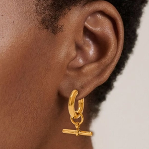 Golden T-bar pendant hoop earrings in stainless steel on a model's ear with soft light